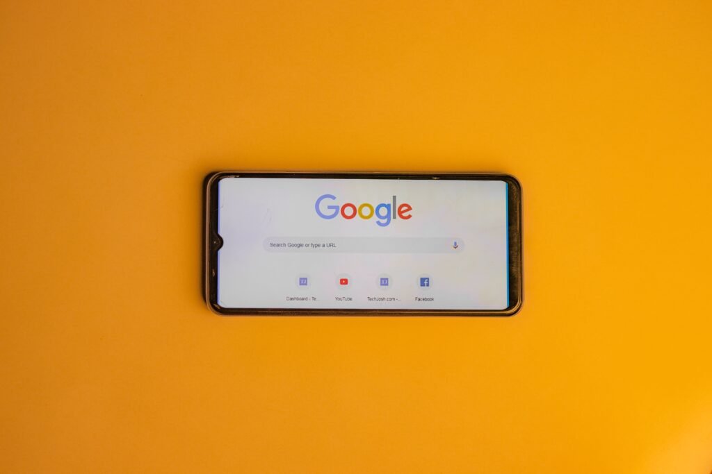 Smartphone displaying Google search page on a vibrant yellow background.
